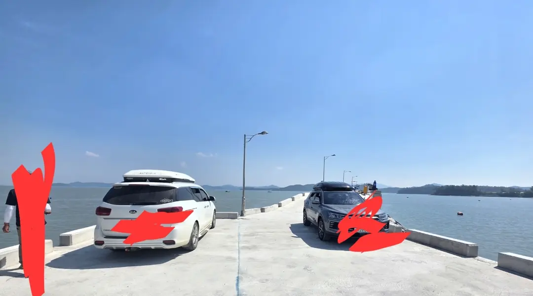 방파제 위에 차 두 대가 서 있고, 그 옆으로 낚시 자리가 붉게 표시되어 있습니다. 바다가 양옆으로 펼쳐지고 멀리 섬이 보입니다